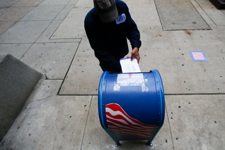 A voter drops a ballot into a mail ballot drop box outside City Hall in May.